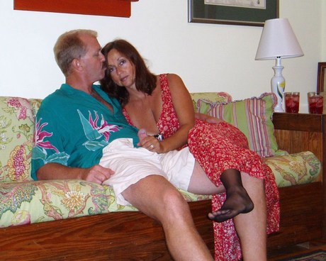 Mature swinger couple sitting closely together on a couch in a relaxed home setting