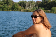 Topless woman wearing sunglasses relaxing beside the lake at clothing-optional Camp NCN North
