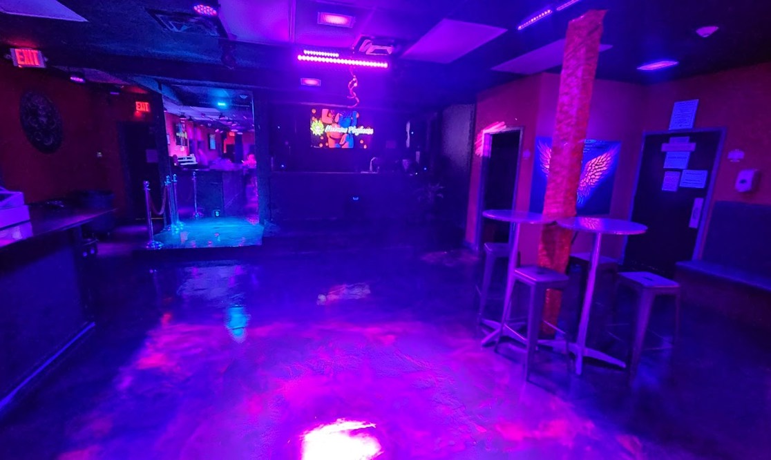 Main club floor with DJ booth, cocktail tables and colorful lighting