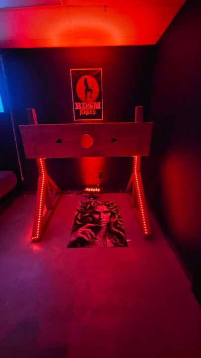 Red-lit BDSM stocks with Medusa artwork