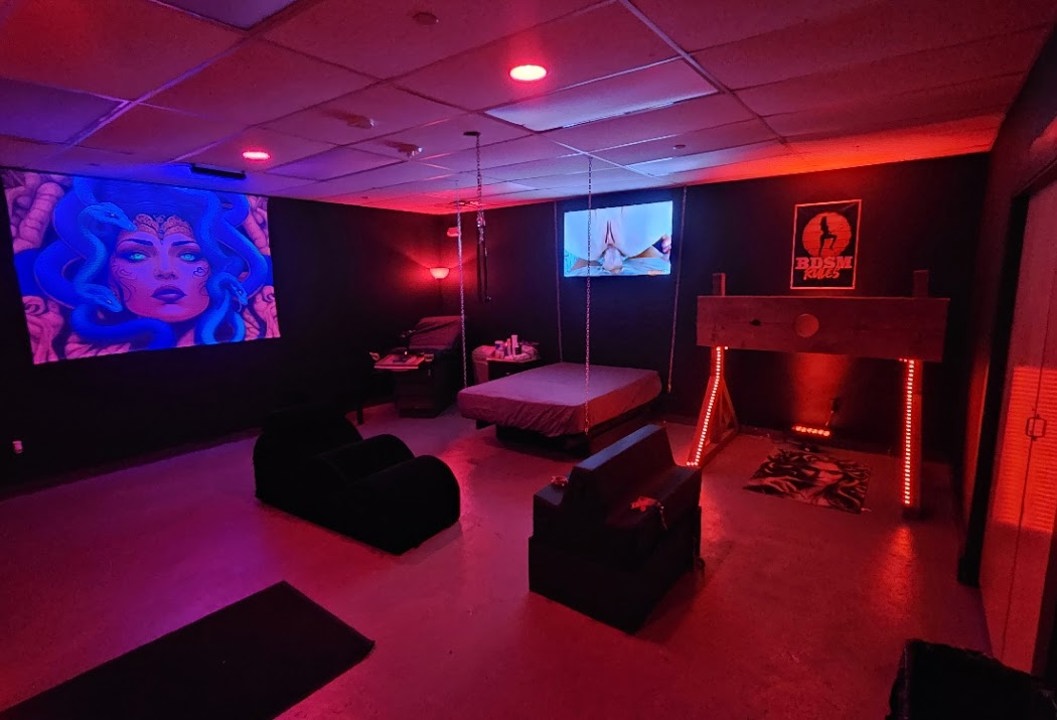 Red-lit BDSM dungeon with play furniture
