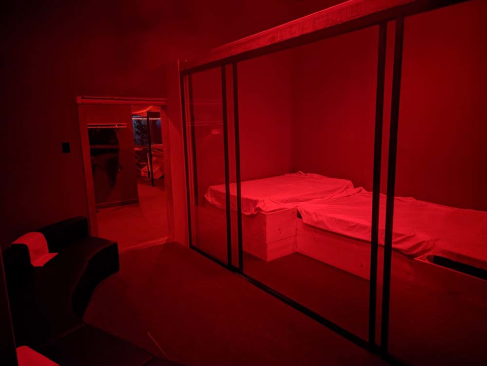 Red-lit private room with padded platforms behind glass