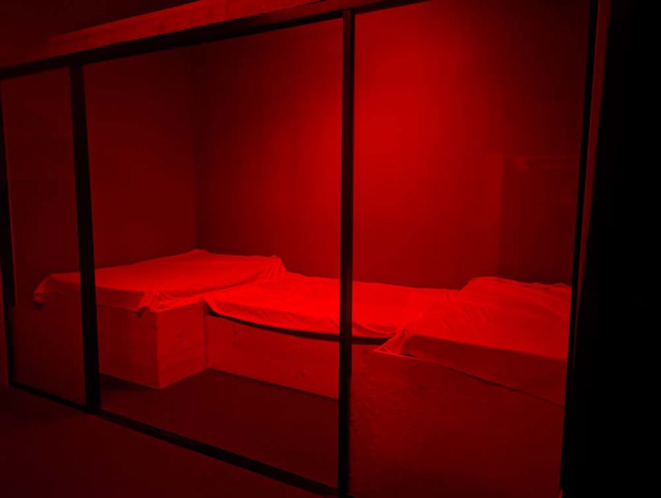 Red-lit private room with padded platforms behind glass panels